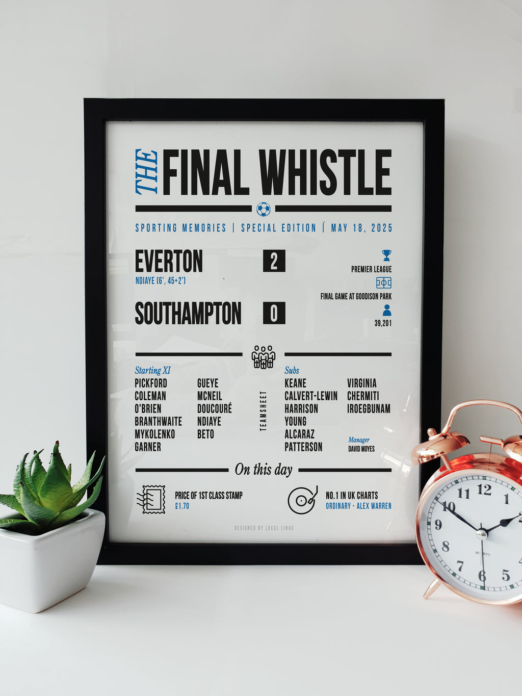 A framed 'Final Whistle' football keepsake print celebrating Everton's 2-0 victory over Southampton in their emotional final game at Goodison Park. The print features the match stats, starting lineup, and "On this day" trivia. It is displayed on a white surface next to a small green potted plant and a classic copper alarm clock. Modern football memorabilia designed by Local Lingo.
