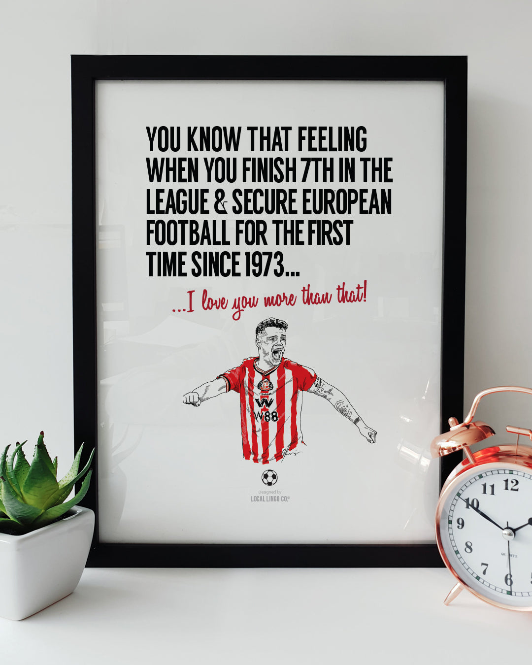 A framed football art print resting on a white surface next to a small green potted plant and a classic copper alarm clock. Bold black text reads "YOU KNOW THAT FEELING WHEN YOU FINISH 7TH IN THE LEAGUE & SECURE EUROPEAN FOOTBALL FOR THE FIRST TIME SINCE 1973..." followed by red text reading "...I love you more than that!". Below is a hand-drawn illustration of Sunderland player Granit Xhaka passionately celebrating in his red and white striped kit. Sunderland football memorabilia designed by Local Lingo.