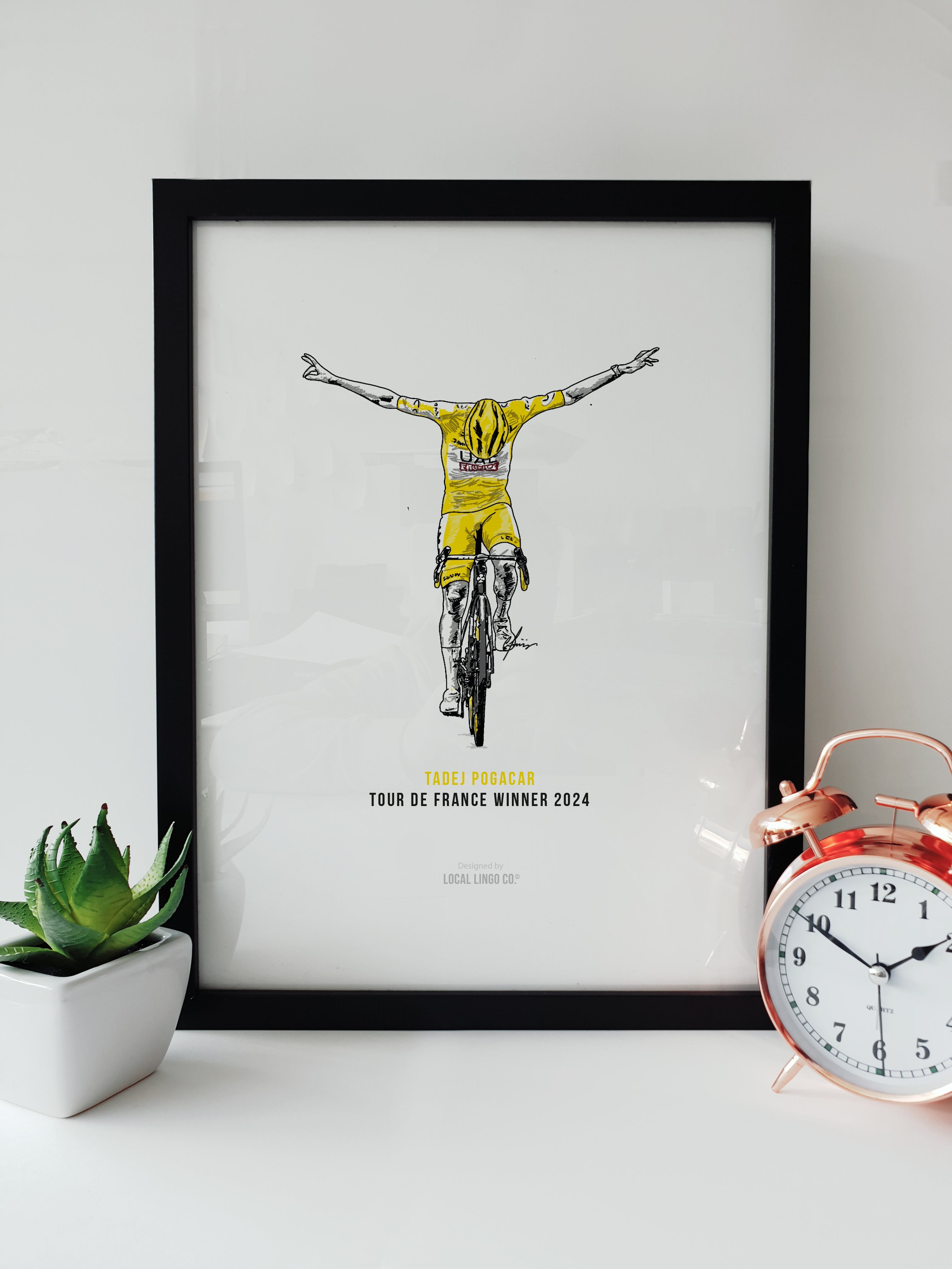 Tadej Pogačar Tour de France Winner 2024 Cyclist Fan Artwork by Local Lingo, featuring an illustration of Pogačar crossing the finish line in the yellow jersey in a black frame.