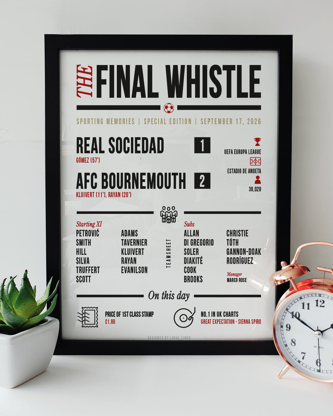 A framed football match report art print resting on a white surface next to a small green potted plant and a classic copper alarm clock. The print is titled "THE FINAL WHISTLE" and displays the match details "REAL SOCIEDAD 1 - AFC BOURNEMOUTH 2" from September 17, 2026. It features the teamsheet, attendance, and "On this day" trivia in black and red text. AFC Bournemouth football print designed by Local Lingo.