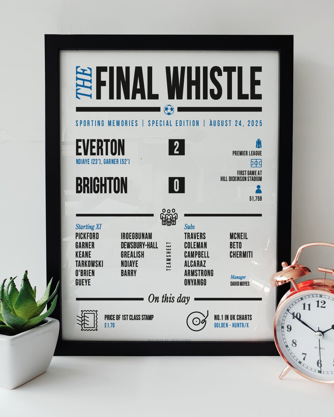 A framed 'Final Whistle' football keepsake print celebrating Everton's 2-0 victory over Brighton in their historic first game at the Hill Dickinson Stadium. The print features the match stats, starting lineup, and "On this day" trivia. It is displayed on a white surface next to a small green potted plant and a classic copper alarm clock. Modern football memorabilia designed by Local Lingo.