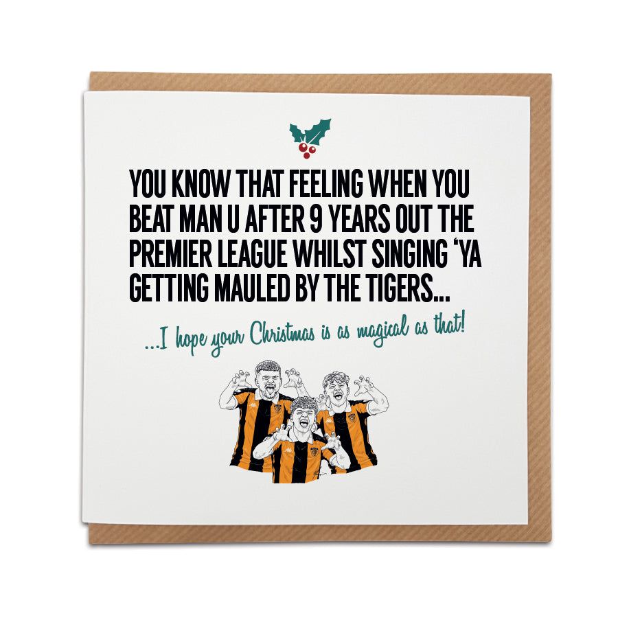 Square Christmas card resting on a brown kraft envelope. A small holly leaf graphic sits above bold black text reading "YOU KNOW THAT FEELING WHEN YOU BEAT MAN U AFTER 9 YEARS OUT THE PREMIER LEAGUE WHILST SINGING 'YA GETTING MAULED BY THE TIGERS..." followed by festive green cursive text reading "...I hope your Christmas is as magical as that!". Below is a hand-drawn illustration of three Hull City fans in amber and black home shirts performing a tiger claw gesture.