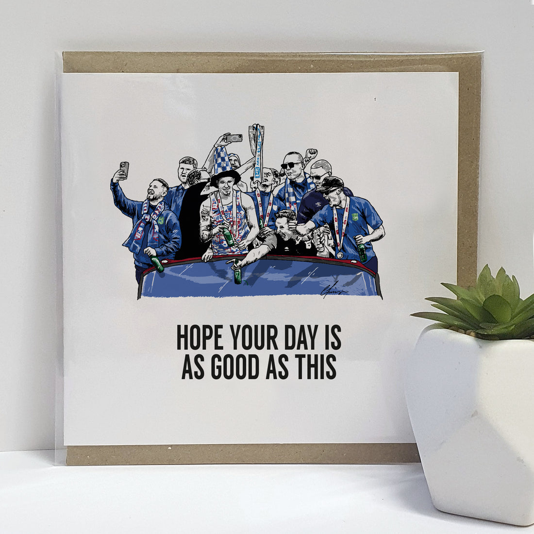 Greeting card featuring Ipswich Town Football Club celebrating their promotion to the Premier League, with the text 'Hope your day is as good as this' above an illustration of the team on a bus, joyously holding up a trophy. designed by local lingo
